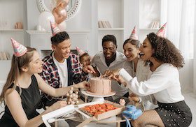A Group of People with Party Hats Sitting at a Table with a Birthday Cake